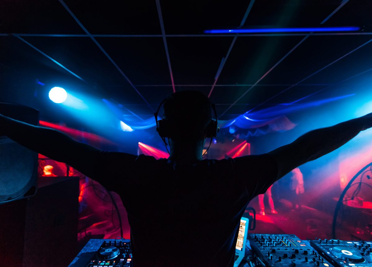 DJ in headphones waving his arms at the party night club silhouette with colored light